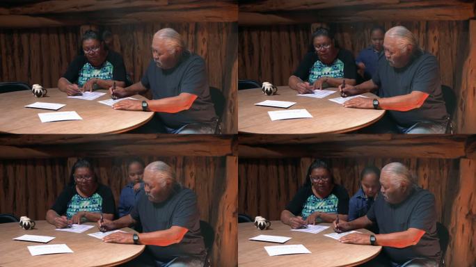年长夫妇在桌旁填写投票邮件，年轻男孩观看学习投票过程