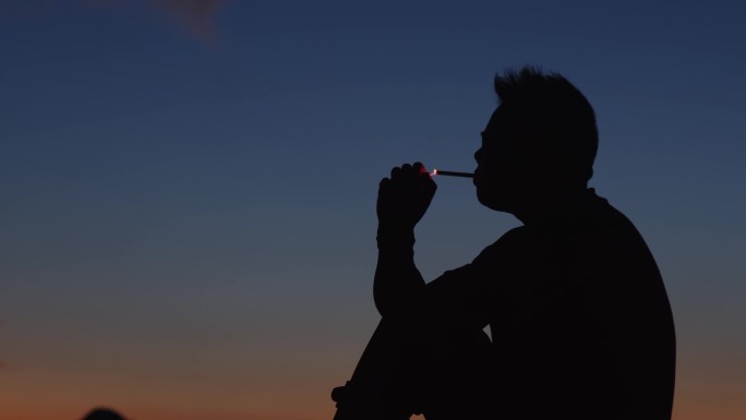 男人坐在山顶抽烟夕阳剪影