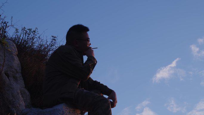 男人坐在山顶孤独抽烟剪影