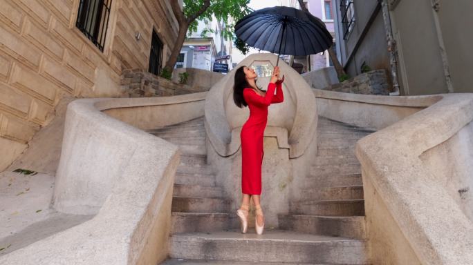 美丽的芭蕾舞演员撑着伞在古老的石头楼梯上跳舞。伊斯坦布尔的卡蒙多楼梯