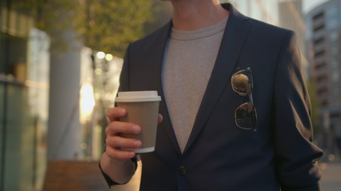 一位穿着蓝色夹克的红发经理正沿着商业中心附近的傍晚街道走着，喝着咖啡