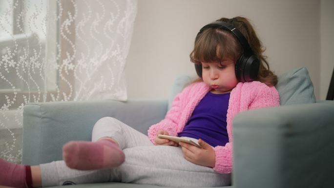 小孩戴着耳机，在家里使用智能手机