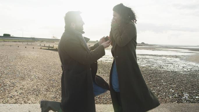 男子在阳光明媚的岩石冬季海滩向女友求婚