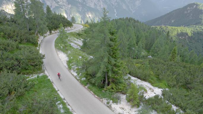 空中女性公路自行车手在森林环绕的山路上骑行