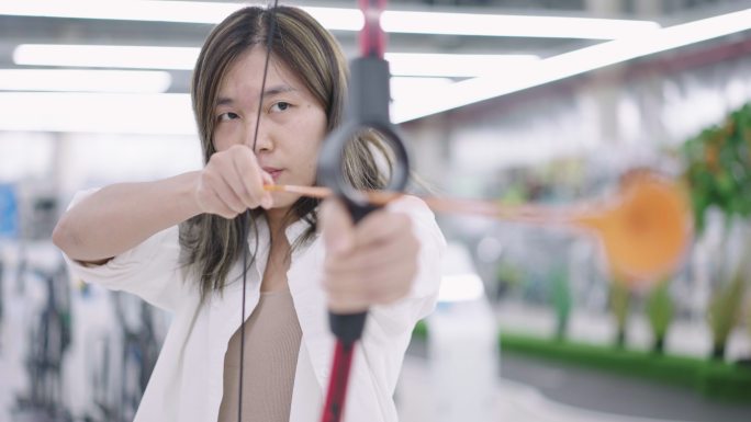 在购物中心运动通道玩玩具射箭弓的亚洲年轻女子