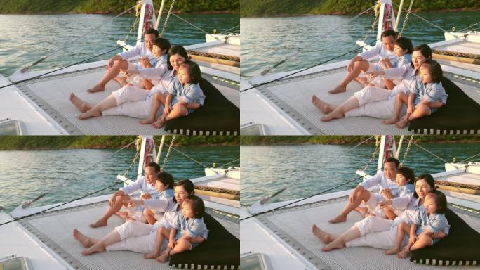 一家人在豪华游艇上度过暑假。他们坐在蹦床上，享受着日落时的谈笑。年轻的母亲和父亲向他们的儿子们伸出手