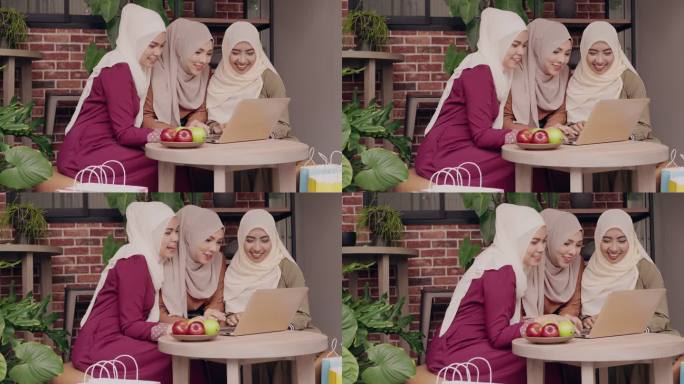 三名年轻的传统穆斯林妇女坐在盖头，一起在咖啡店网上购物，旁边放着一些水果。中间的一个女孩和她的朋友滚