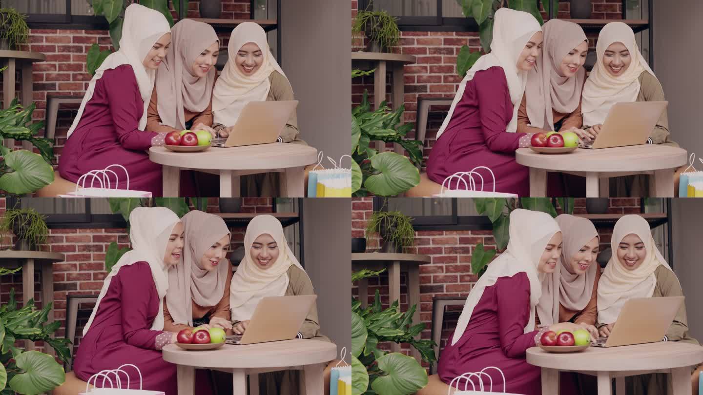 三名年轻的传统穆斯林妇女坐在盖头，一起在咖啡店网上购物，旁边放着一些水果。中间的一个女孩和她的朋友滚