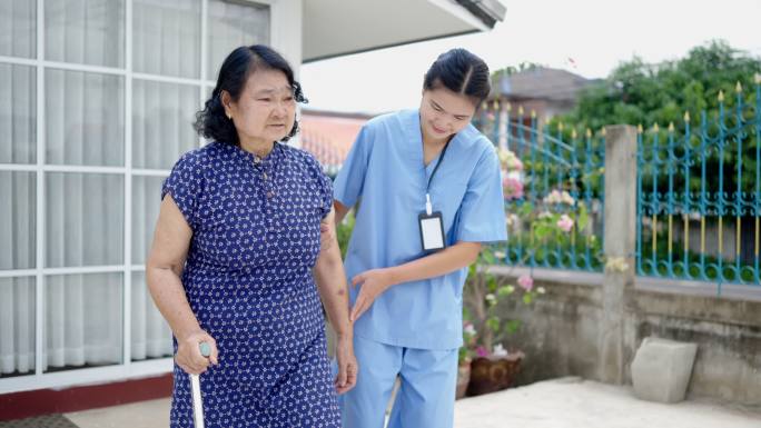 女护士帮助老人用拐杖走路，理疗。