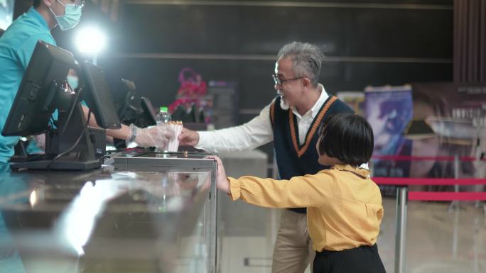 亚裔中国祖父孙女在电影院电影放映前使用非接触式付款购买爆米花