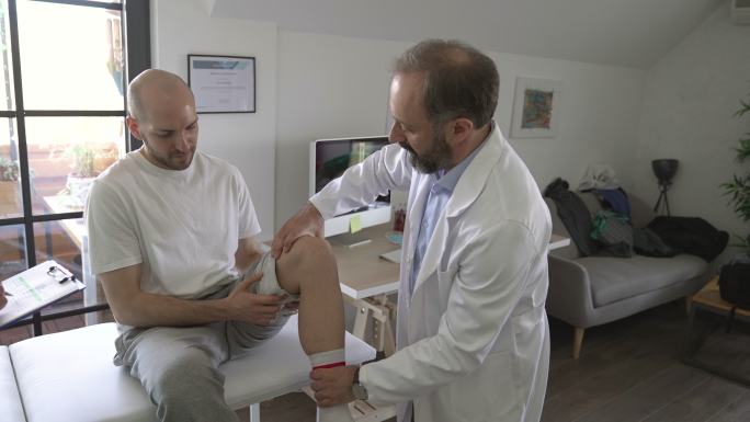 物理治疗师和他的助手在医生办公室与老年患者谈论他的膝盖受伤