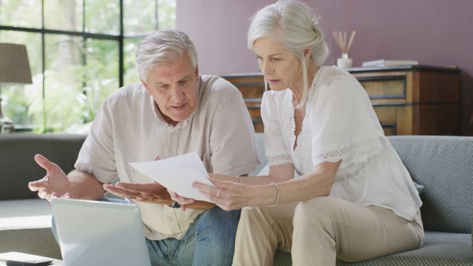 一对年长的夫妇在家里使用笔记本电脑时，计划财务，支付账单，看起来很不开心。一个成熟的男人和女人在网上