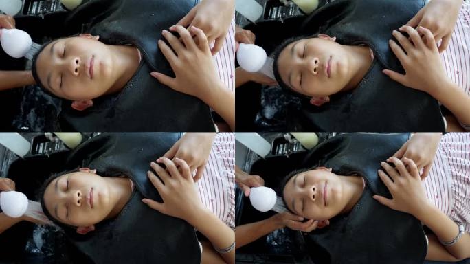一位亚洲女孩躺在洗发水椅上，闭上眼睛，母亲在洗头，这是她的生活方式理念。