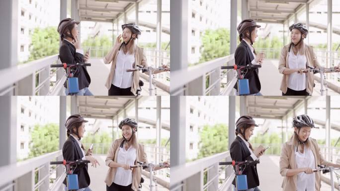 一位戴着头盔的亚洲女商人在桥上拖着自行车去上班，她正在和她的朋友会面，她手里拿着电动踏板车，用手机聊