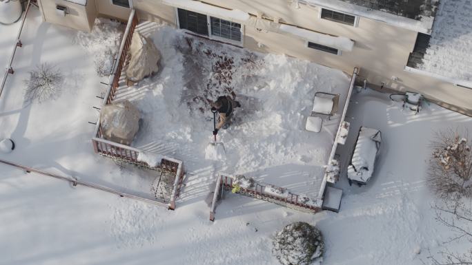 一位成年男子在冬季降雪后用铲子清理走廊上的积雪。无人机慢动作视频正上方的鸟瞰图。