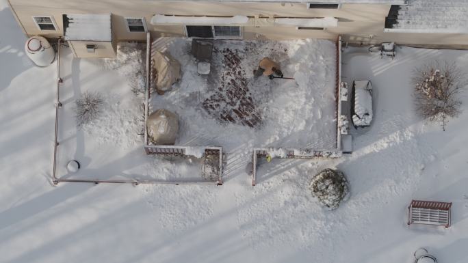 一位成年男子在冬季降雪后用铲子清理走廊上的积雪。无人机视频正上方的鸟瞰图。