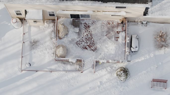 一位成年男子在冬季降雪后用铲子清理走廊上的积雪。鸟瞰图直接在无人机加速的时间轴式视频上方。