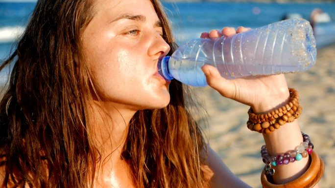 一个口渴的女孩在海滩上喝冷水的慢动作特写镜头