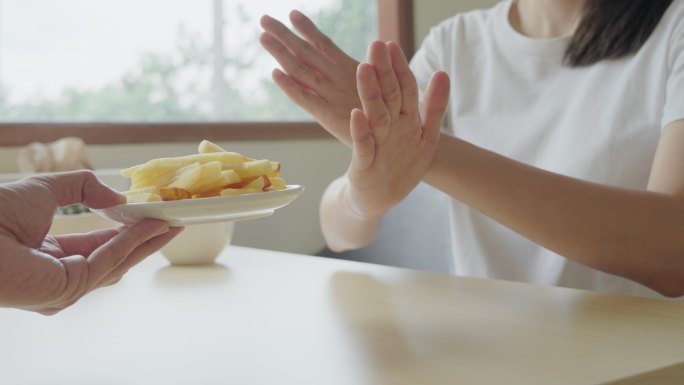 饮食概念。健康女性用手拒绝不健康的食物，如甜甜圈或甜点。苗条女性选择健康食品和高维生素