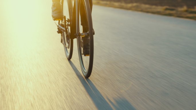 男性公路自行车手在空旷的田野上疾驰的背光剪影。春季日落