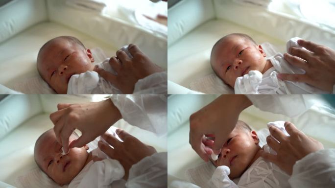 婴儿护理者用湿棉球清洁新生儿面部