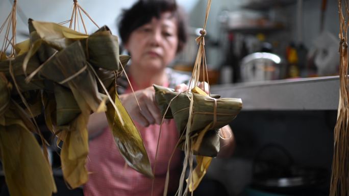 一位亚洲华裔高龄妇女在厨房里准备粽子，放入配料并将其包装起来，为端午节做准备