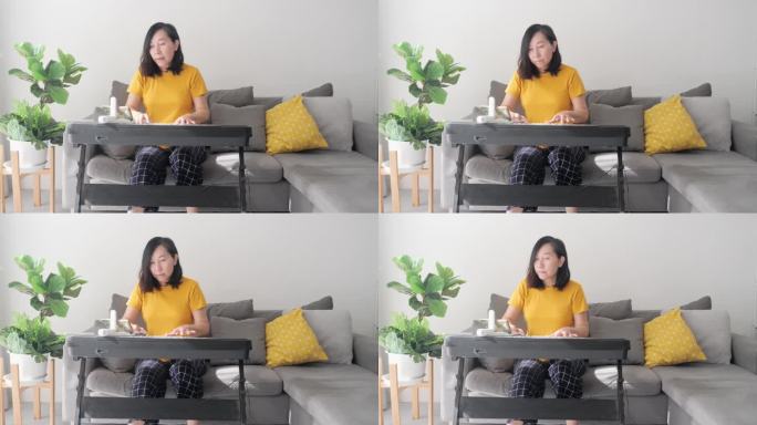 亚洲成年母亲在家靠窗的沙发上学习使用手机应用程序弹奏键盘乐器，生活方式理念。