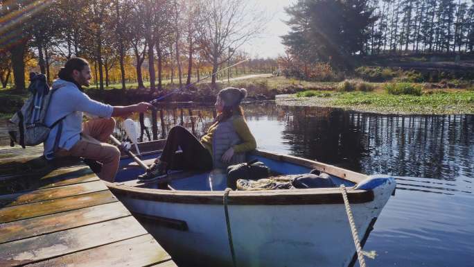 年轻夫妇在阳光明媚的秋湖划船钓鱼放松