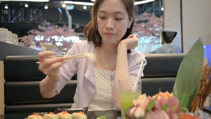 泰国曼谷餐厅的亚泰中国商务女性穿着现代服装，手持筷子吃鳄梨寿司和新鲜的沙西米高级套餐