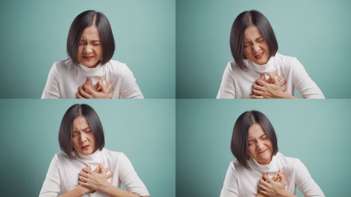 一名亚洲女性因胸痛而生病，在蓝色背景下被隔离。4K视频。医疗保健概念。