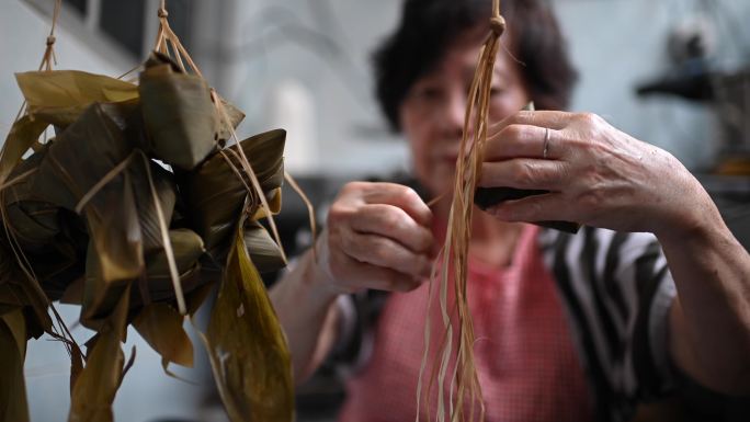 一位亚洲华裔高龄妇女在厨房里准备粽子，放入配料并将其包装起来，为端午节做准备