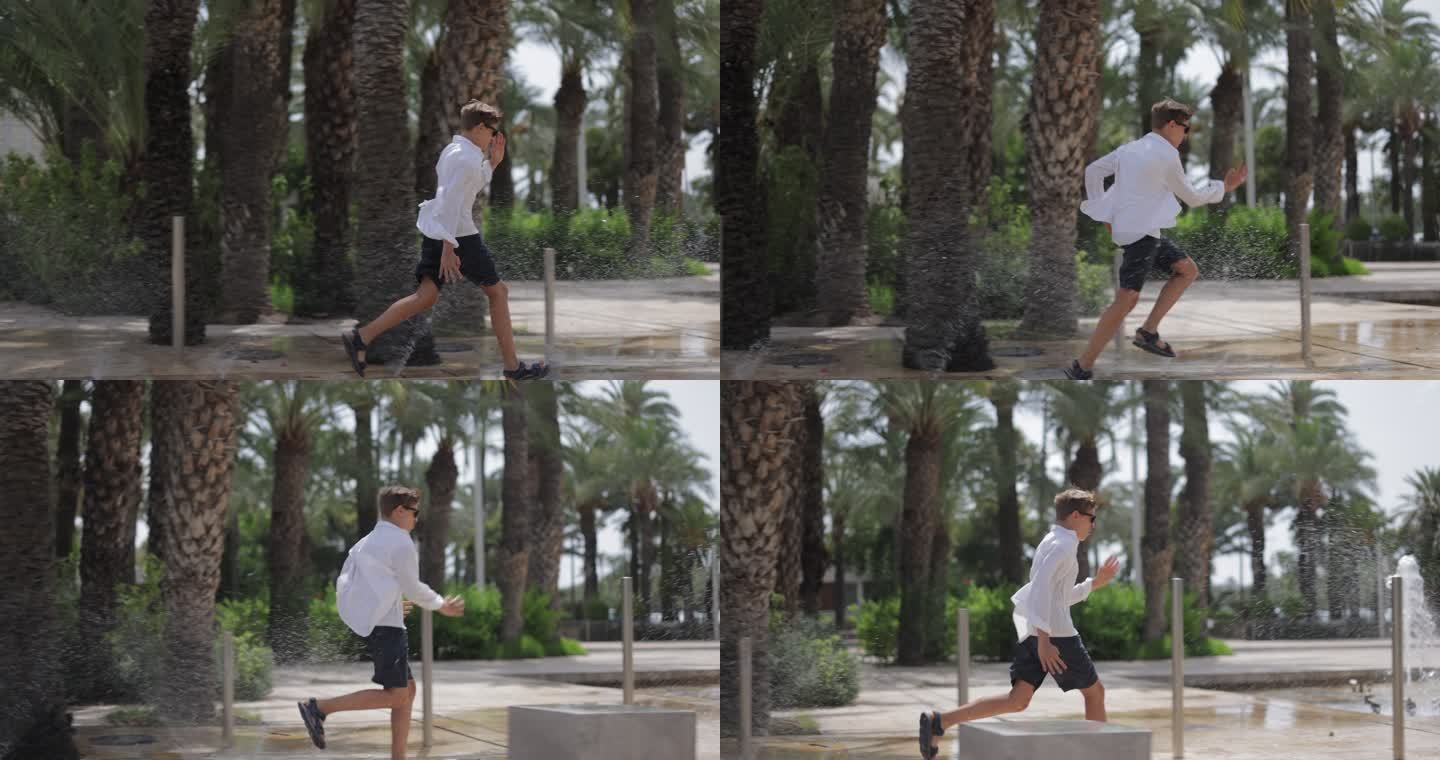一个十几岁的男孩跑过城市街道上的洒水喷泉。