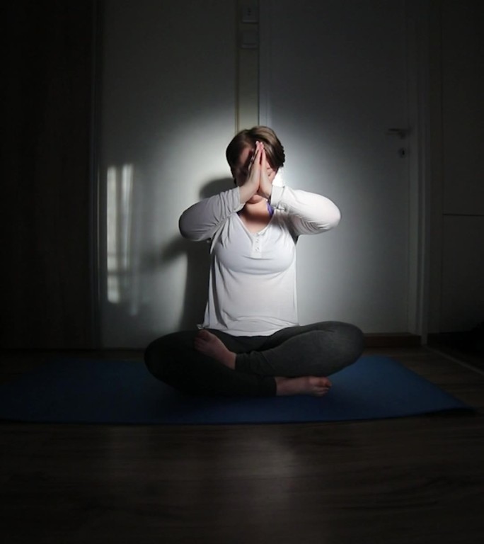 一位女士在她的公寓里练习瑜伽。日落时公寓的灯光效果。
