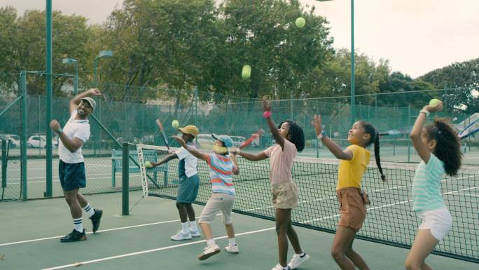 一群孩子和教练一起打网球。一名男子教快乐、可爱、多样化的网球运动员在球场上使用球拍