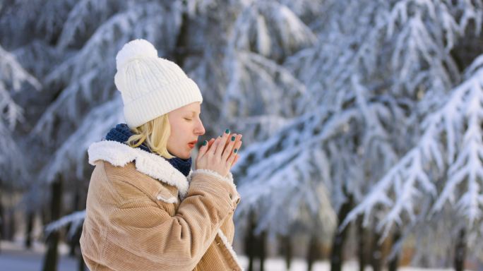 一个在白雪中冻僵的女人试图用手吹暖和自己