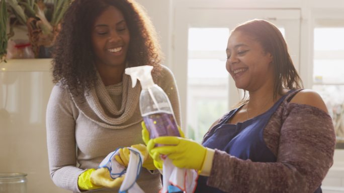 母亲和女儿用喷雾瓶和手套清洁厨房