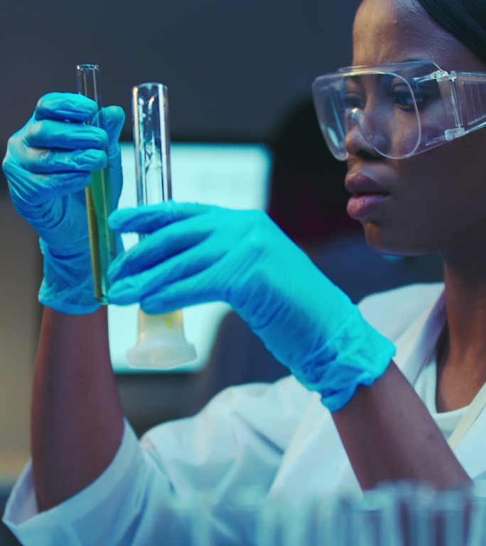 一位年轻的非裔美国医学生身穿白色实验服，在现代实验室里用烧瓶工作的侧面特写