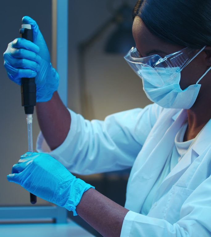 一位年轻的非裔美国实验室医生身穿白色实验服，为显微镜检查准备涂片的特写镜头