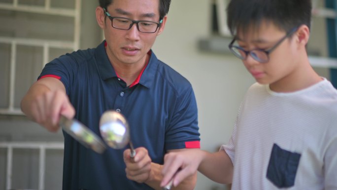 周末，亚裔中国父亲在潮湿的厨房后院教儿子做饭准备晚餐