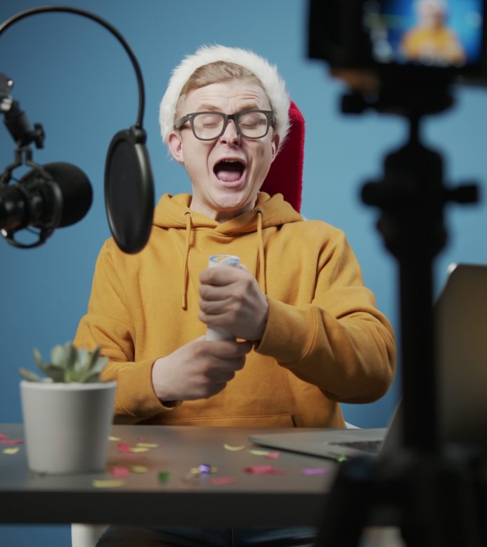 一个欢快的年轻博主为他的频道拍摄圣诞场景，在工作室里引爆了一个蓝色背景的圣诞饼干
