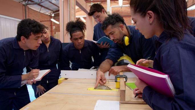 拉丁美洲男老师向他的学生解释如何在木工实验室工作，而他们都在专心致志
