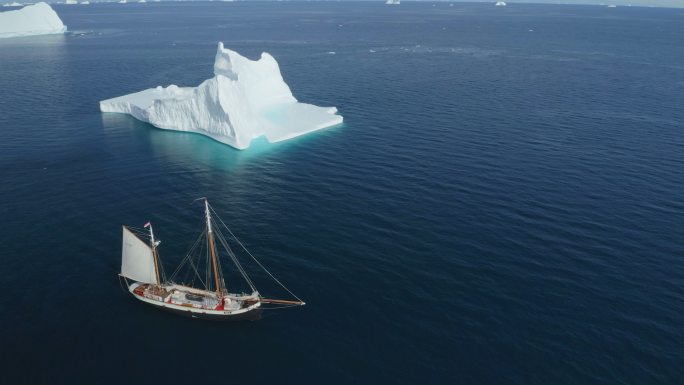 船沿着冰山停泊在阳光明媚的蓝海格陵兰岛