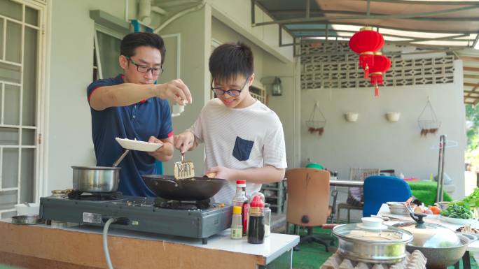 周末，亚裔中国父亲和儿子在潮湿的厨房后院一起做饭准备晚餐