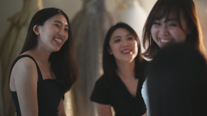 中国亚裔新娘在伴娘的簇拥下试穿婚纱在婚纱店欣赏婚纱的美丽