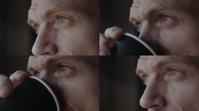 一个深思熟虑的人在黎明时站在窗前喝咖啡。男人眼睛的特写。