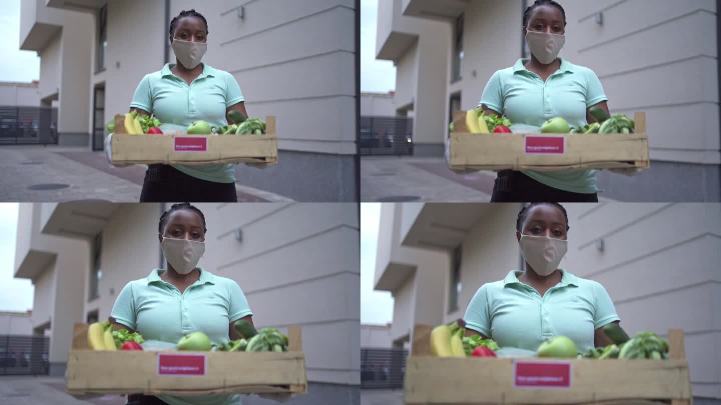 黑人女性志愿者手持装有新鲜蔬菜的板条箱，在冠状病毒大流行期间为有需要的人运送蔬菜