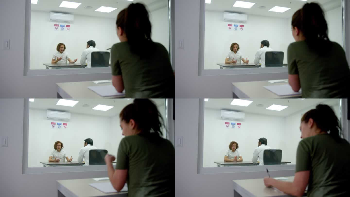 女学生一边做笔记，一边观察一名男性患者在盖塞尔室接受精神病医生的采访