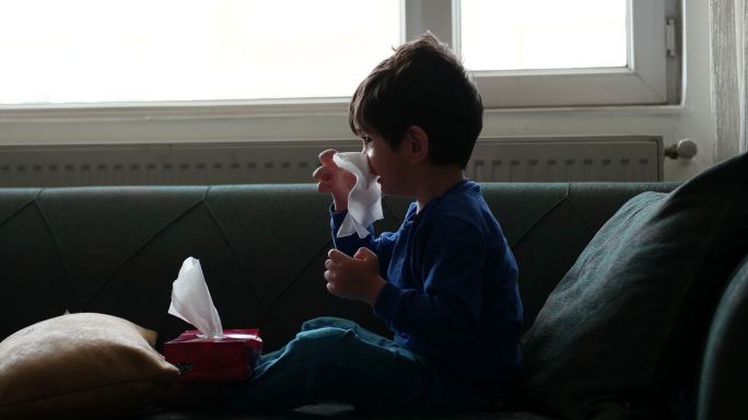微笑的学龄前儿童，用面巾纸治疗感冒或鼻炎