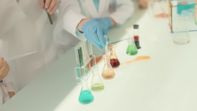 孩子们在实验室里做科学实验。用吸管倒入多色液体。闭合