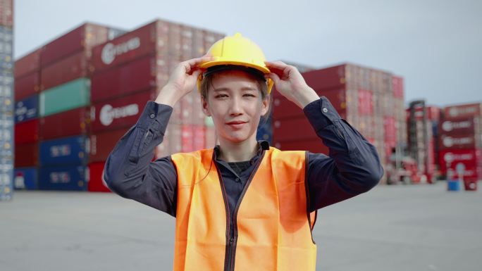 货物管理部亚洲妇女身穿安全防护服，双手交叉站在大型货柜前的肖像。